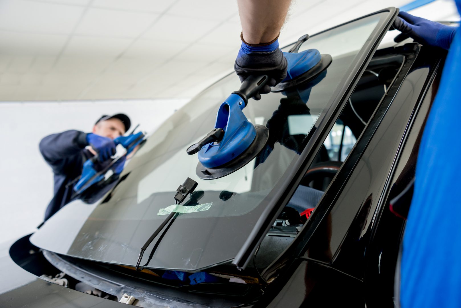 Automobile special workers replacing windscreen or windshield of a car in auto service station garage.